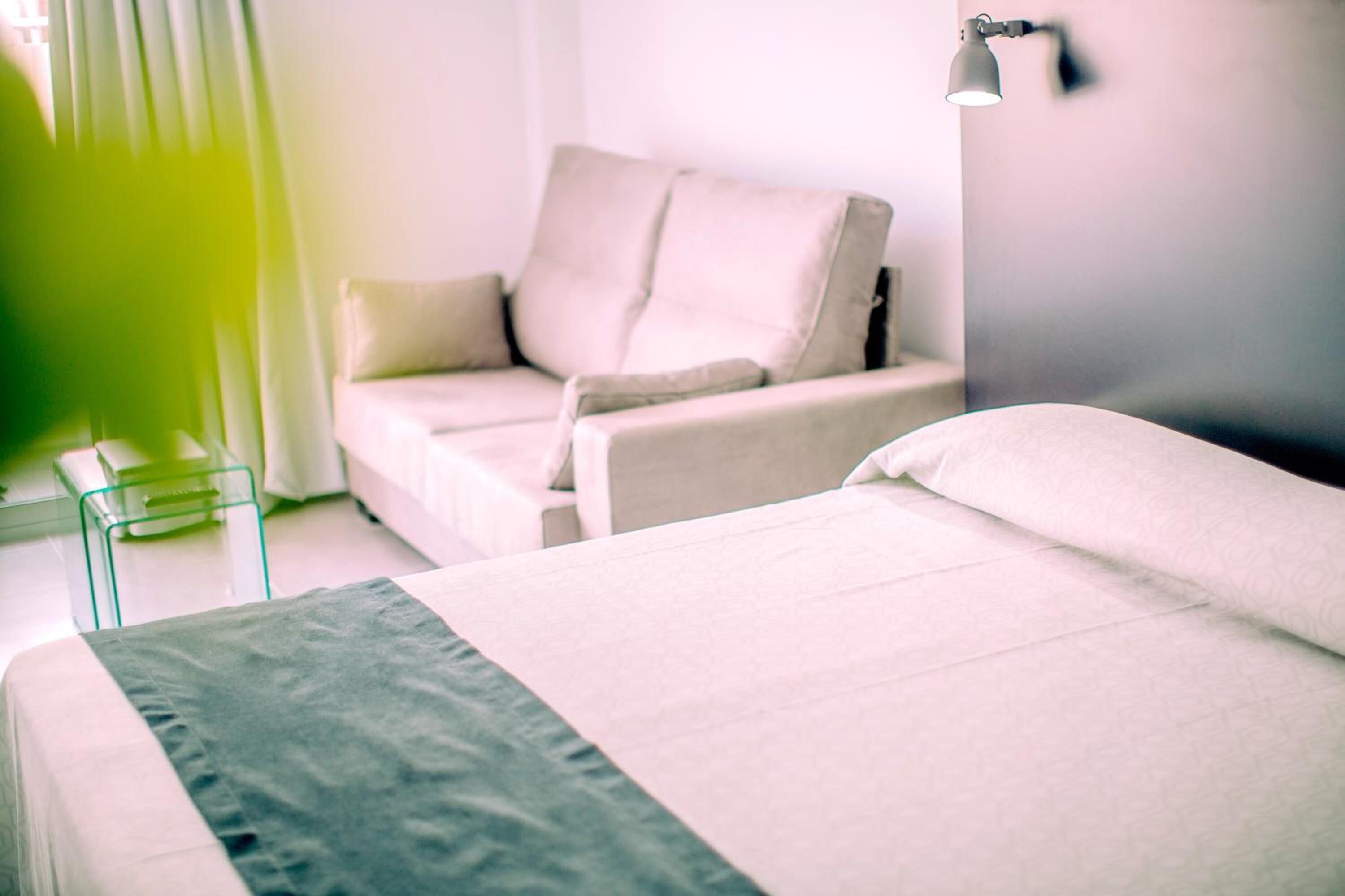 A modern hotel room with a bed, a chair, and a bedside table.