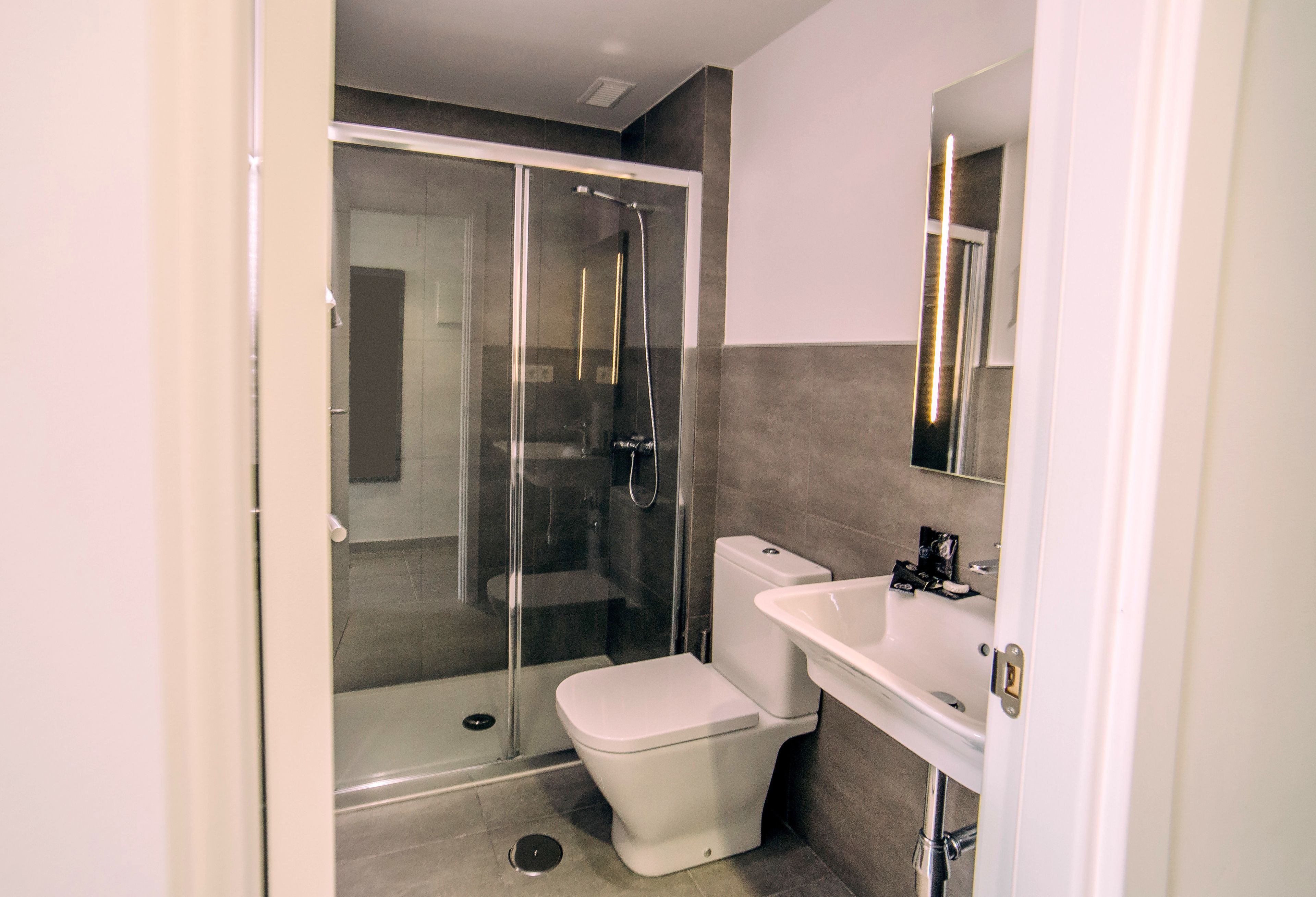 A modern bathroom with a glass-enclosed shower, a white toilet, and a sink with a mirror above it.