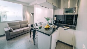 A modern kitchen with a built-in microwave, a dining area with a sofa and bar stools, and a large window providing natural light. - Mannix Urban Apartments (Las Palmas de Gran Canaria)