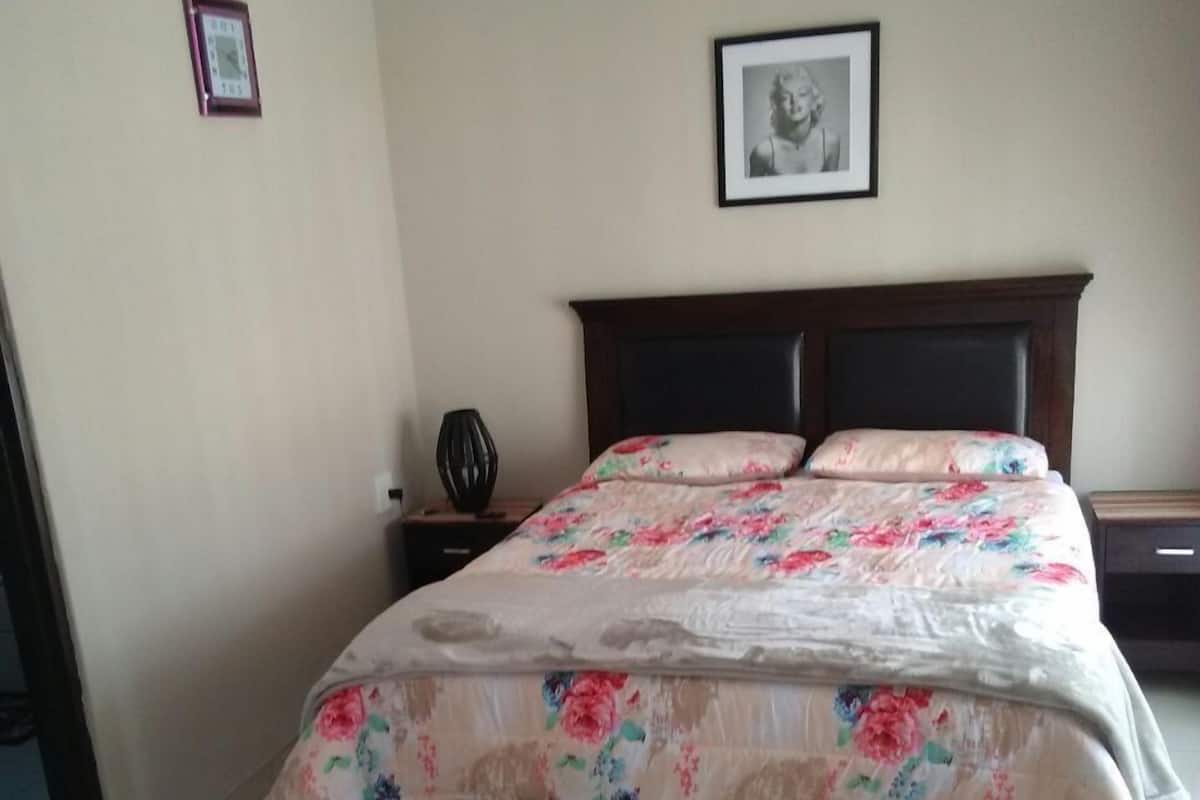 Een slaapkamer met een bed, een nachtkastje, een lijst met een foto aan de muur en een klok.