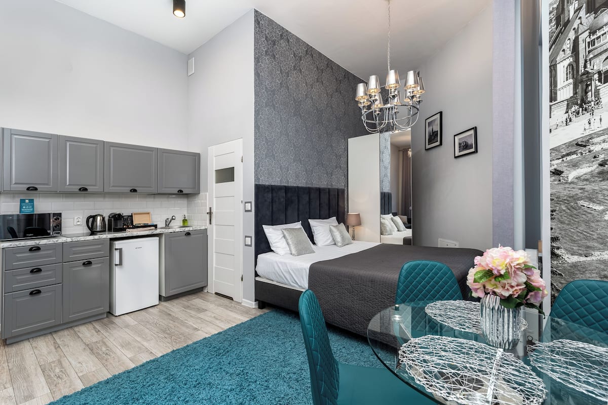 Una habitación de hotel moderna con kitchenette, una cama grande, un área de comedor y un espejo amplio.