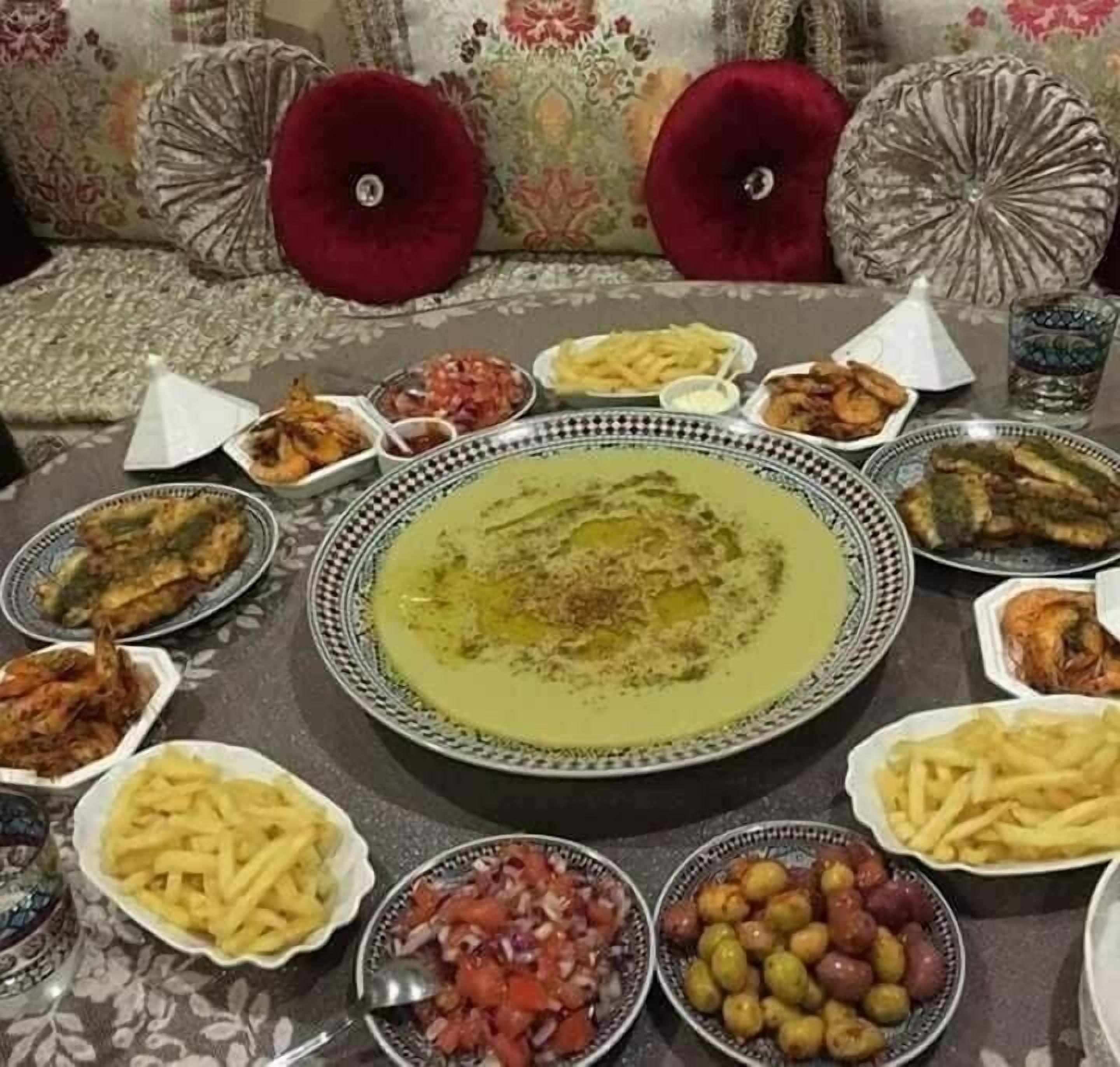 A dining table with various dishes, including a central bowl of soup, surrounded by plates of fries, olives, and other food items.