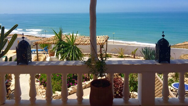 Een balkon met uitzicht op de oceaan, plantenbakken en een strand in de verte.