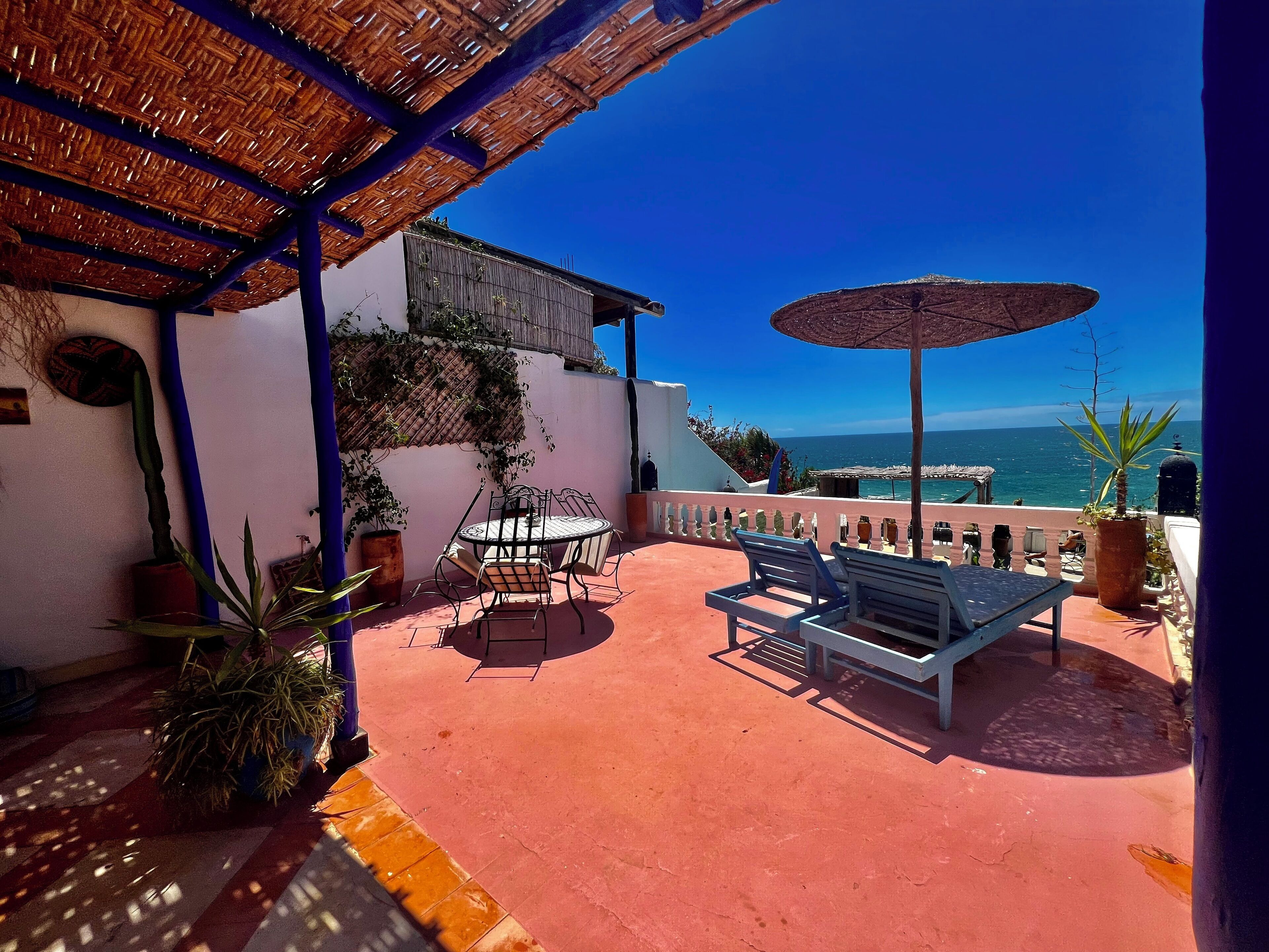 An outdoor patio with a table and chairs, a bench, and a view of the ocean.