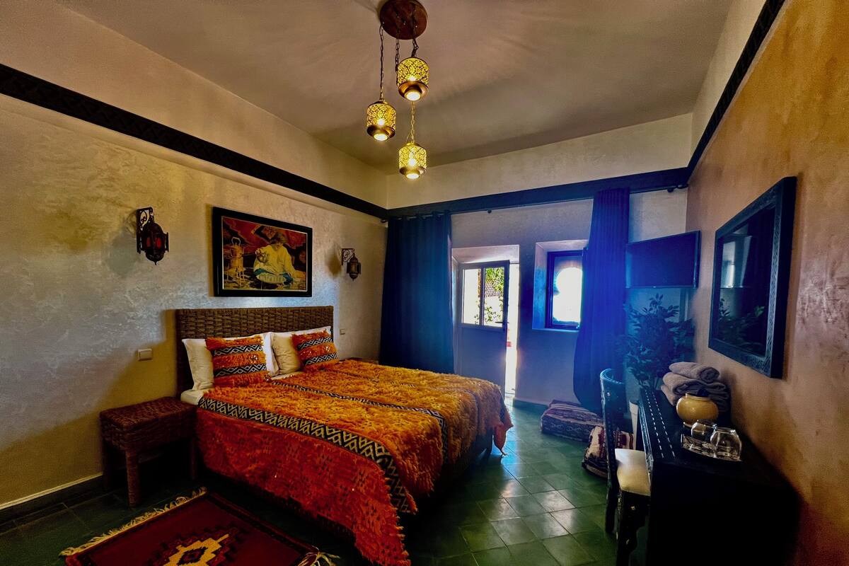 Un dormitorio con cama, mesita de noche, lámpara, alfombra y ventana.