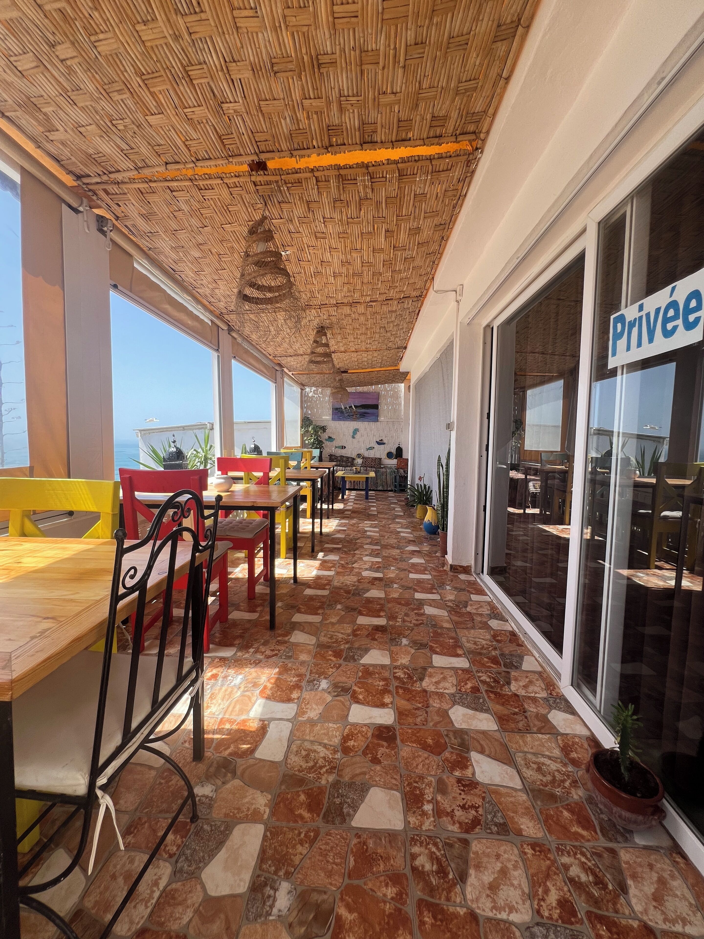 A covered outdoor seating area with stone flooring, tables, and chairs.