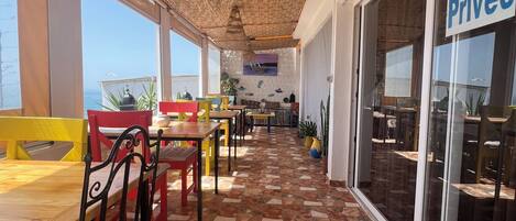 A covered outdoor seating area with stone flooring, tables, and chairs.