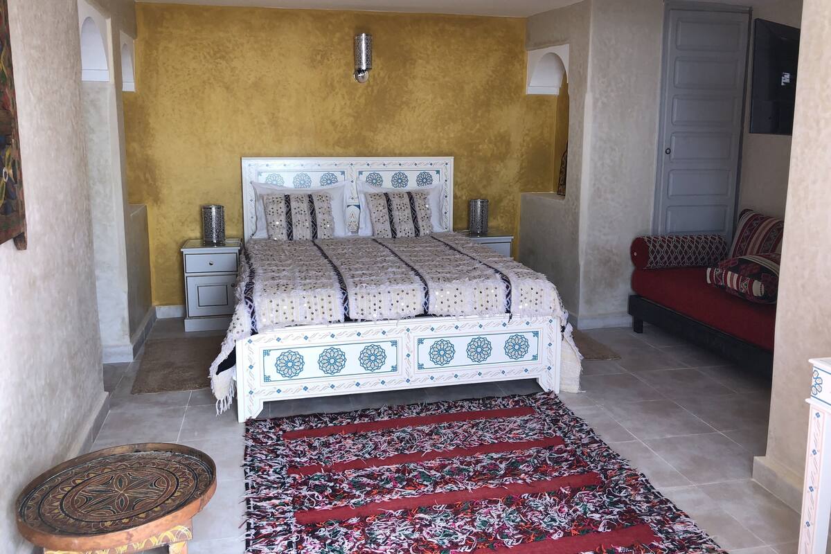Un dormitorio con una cama, mesitas de noche, un sofá rojo y una alfombra estampada.