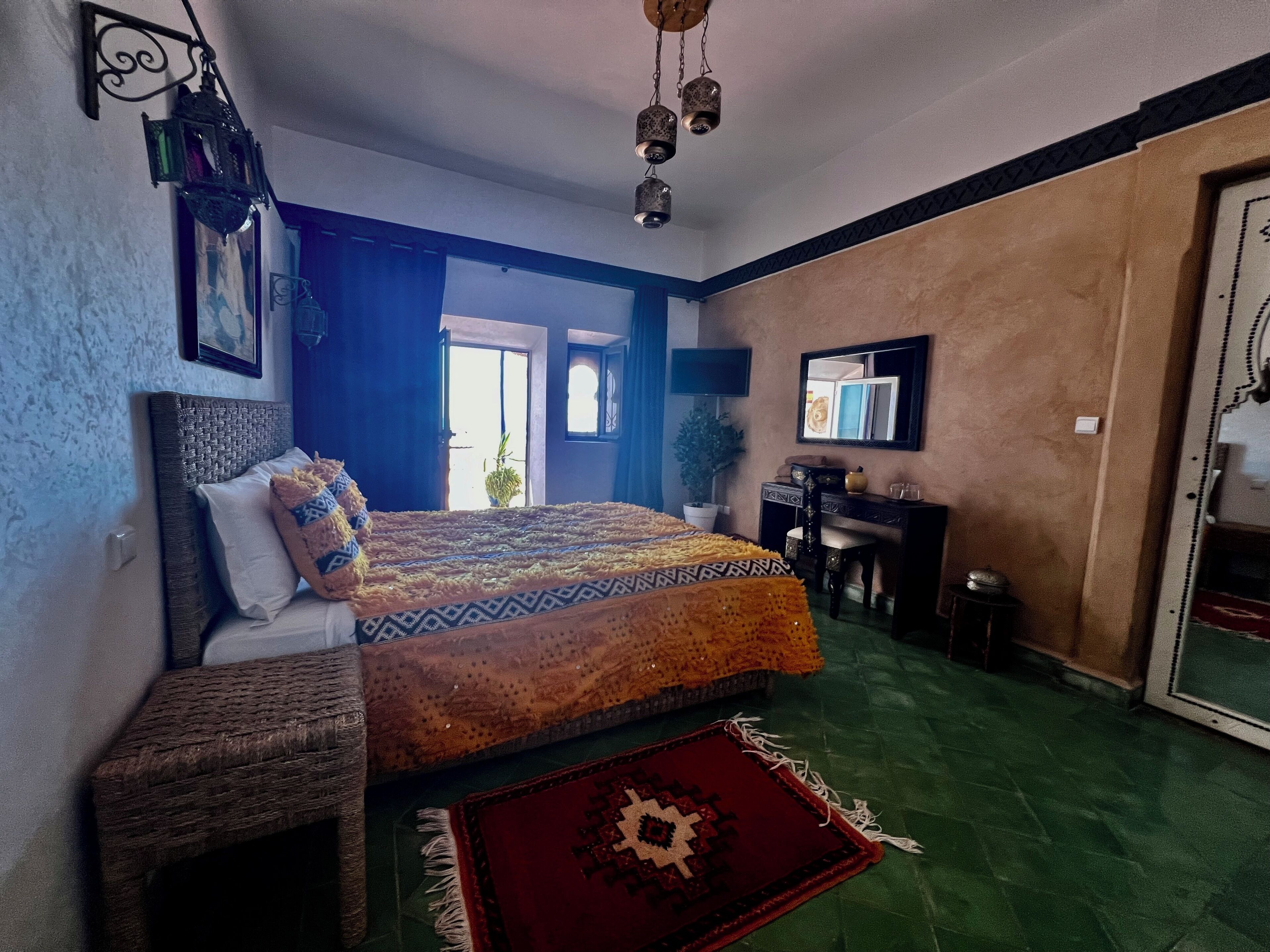 Ein Schlafzimmer mit Bett, Schreibtisch, Stuhl, Fernseher und Fenster.