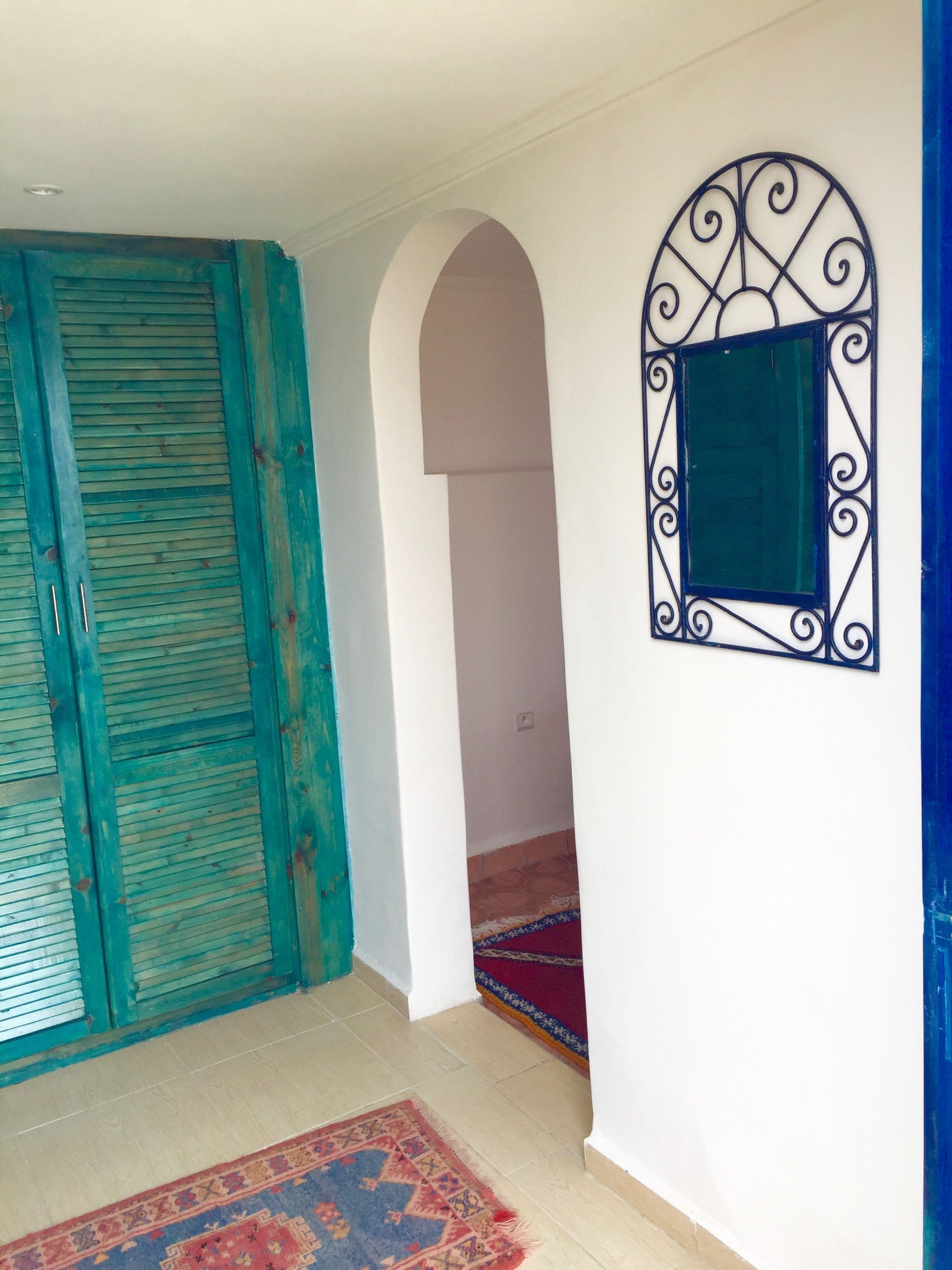 A room with a teal-colored door, a patterned rug, and a decorative metal-framed window.