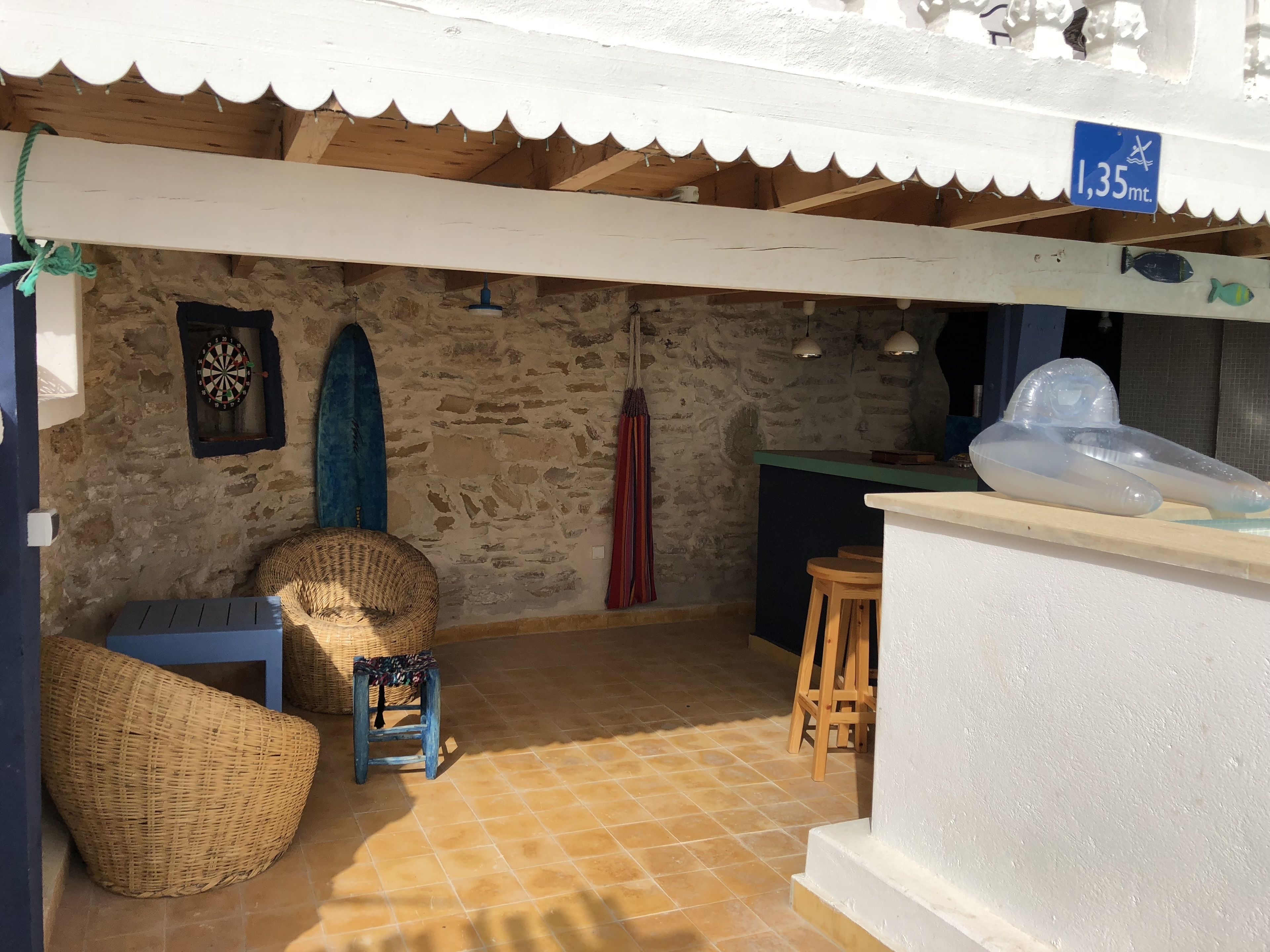 Una habitación con pared de piedra, dardos, una tabla de surf y una silla de playa.