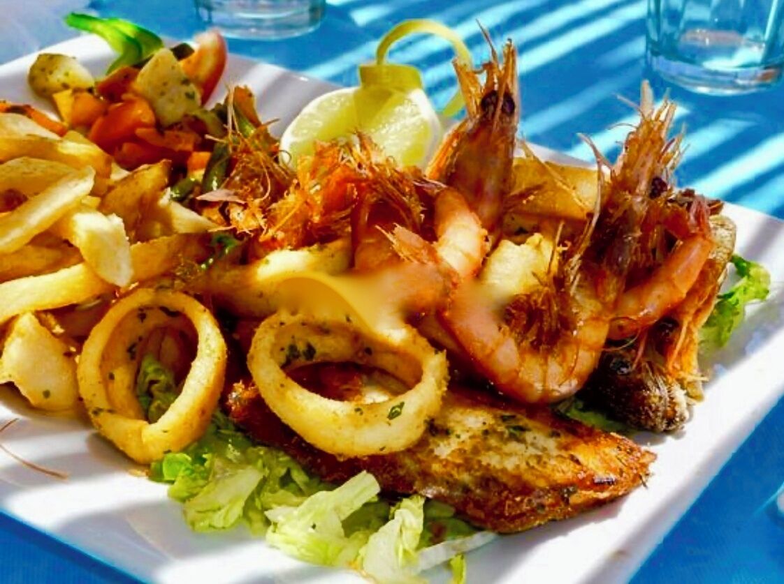 A seafood platter with shrimp, squid rings, and potatoes on a white plate.