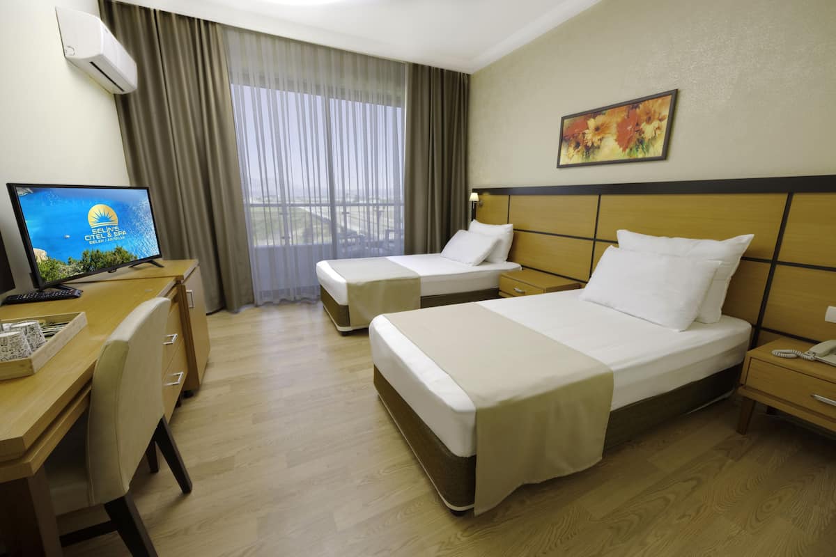 A hotel room with two beds, a desk with a computer, a chair, and a window with curtains.