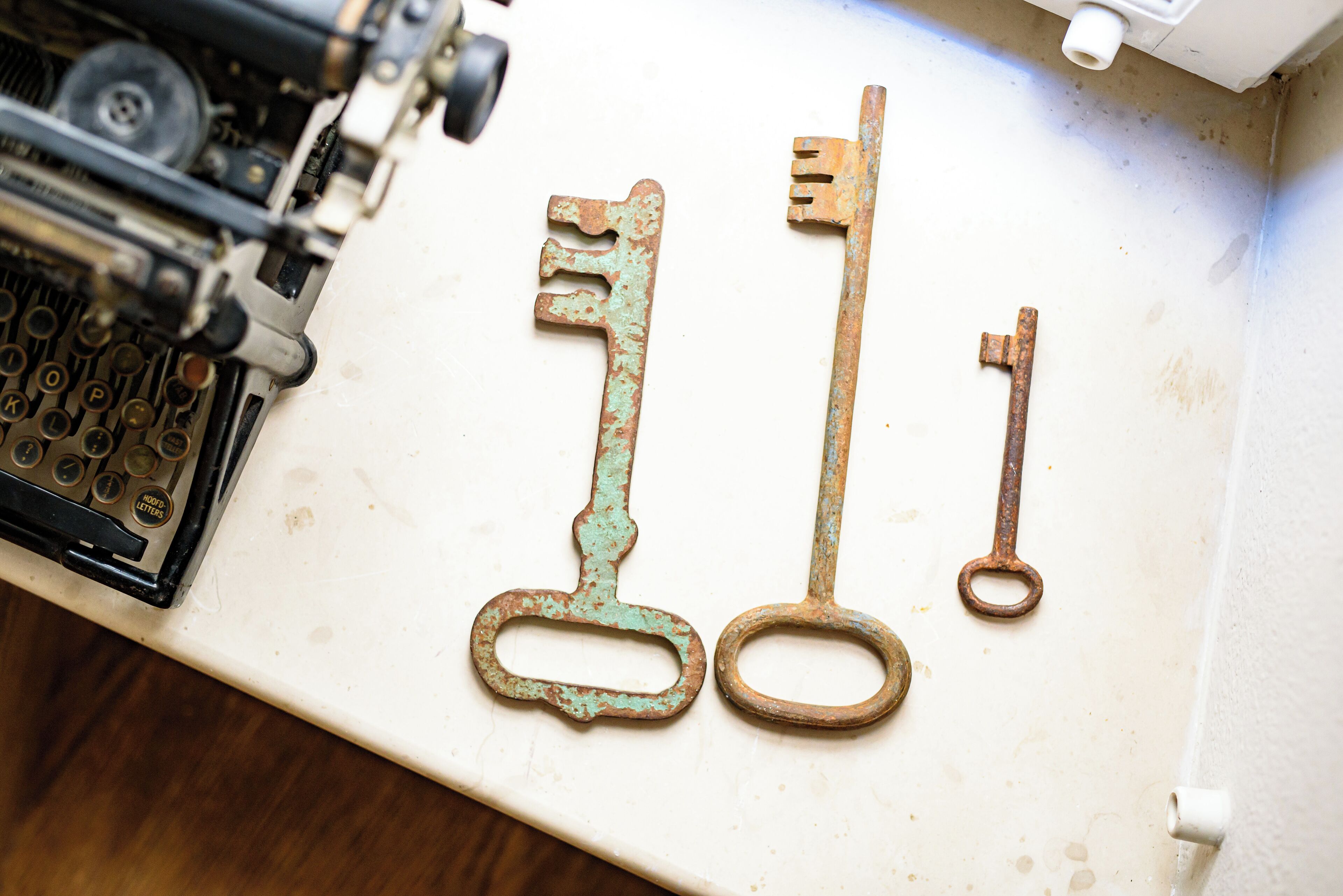 Une machine à écrire ancienne et trois clés d’époque, posées sur une surface blanche.