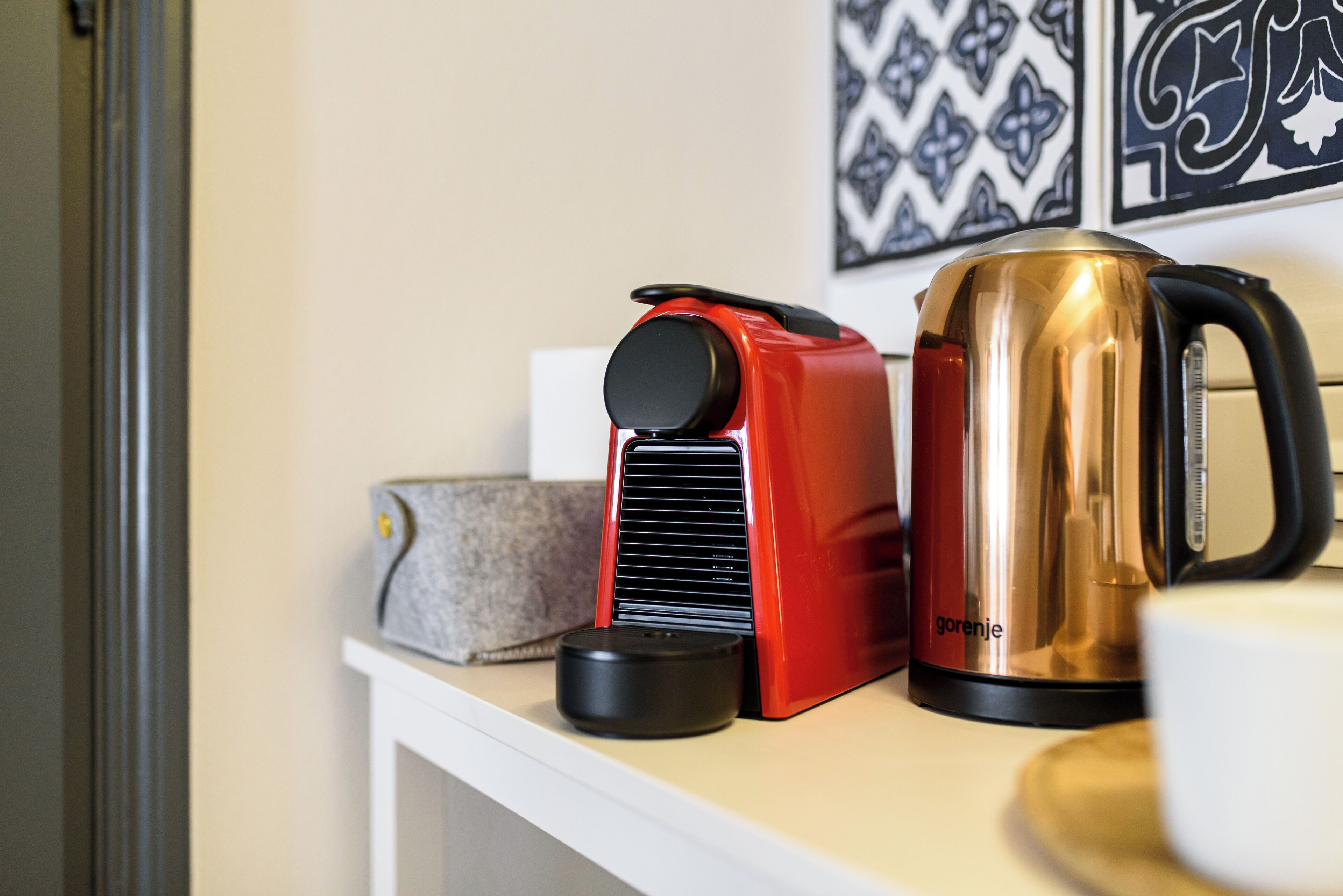 A kitchen counter with a red electric kettle, a stainless steel coffee pot, and a black electric kettle.