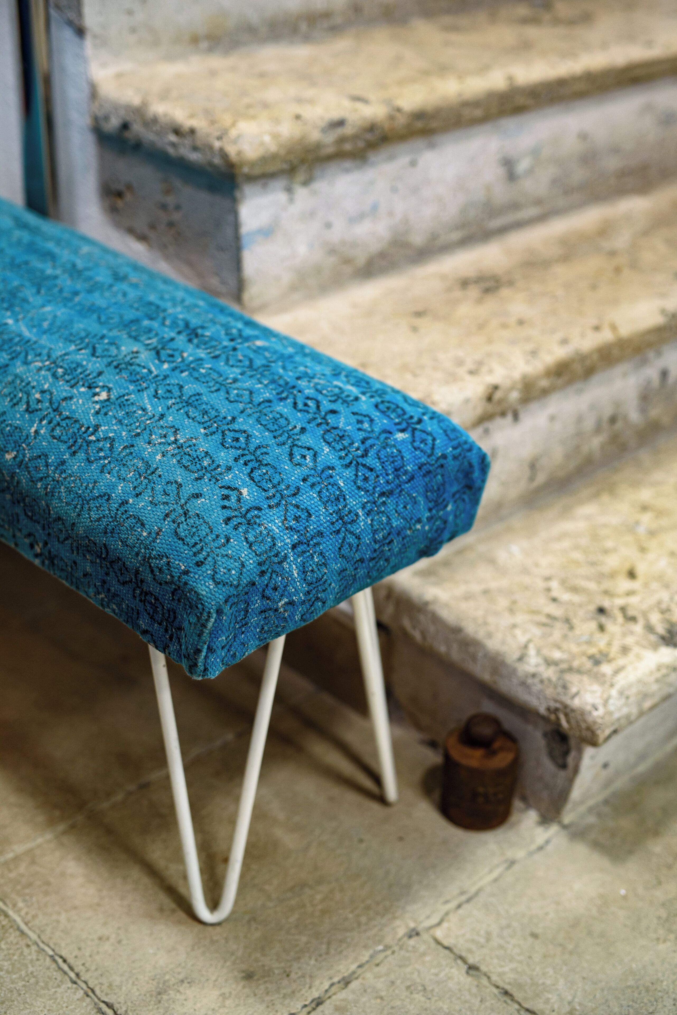 Un banco azul con estampado y patas blancas, ubicado en una escalera de piedra.