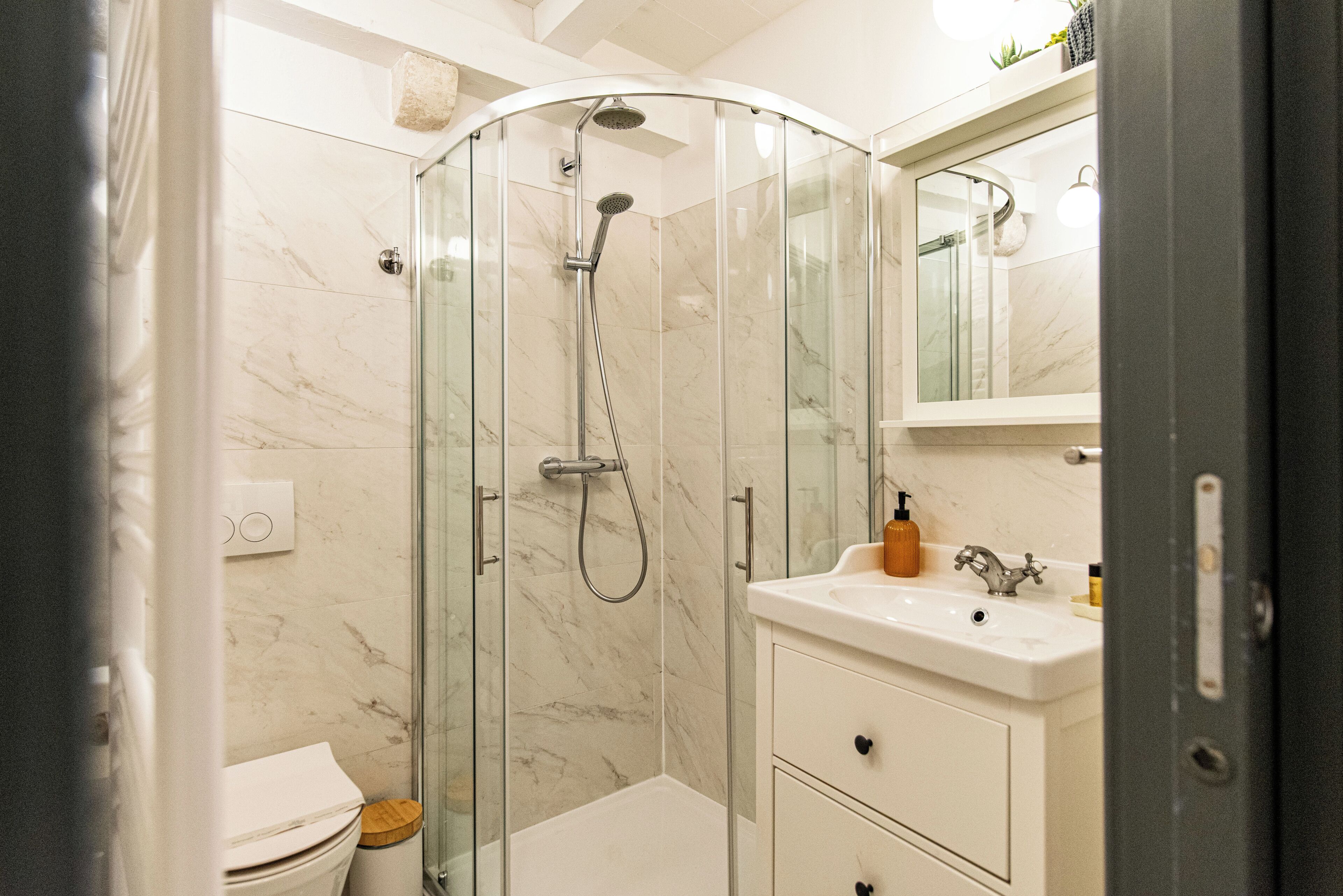 Une salle de bain moderne avec une douche à parois de verre, un lavabo blanc et un miroir au-dessus du lavabo.