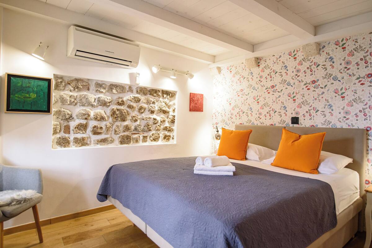 A bedroom with a stone wall, a bed with orange pillows, and a blue bedspread.