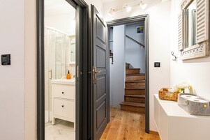 Un pasillo con una escalera de madera, un lavamanos blanco y un espejo.
