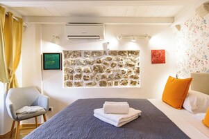 Quarto de hotel com uma cama, uma cadeira, aparelho de ar condicionado, parede de pedra e papel de parede floral.