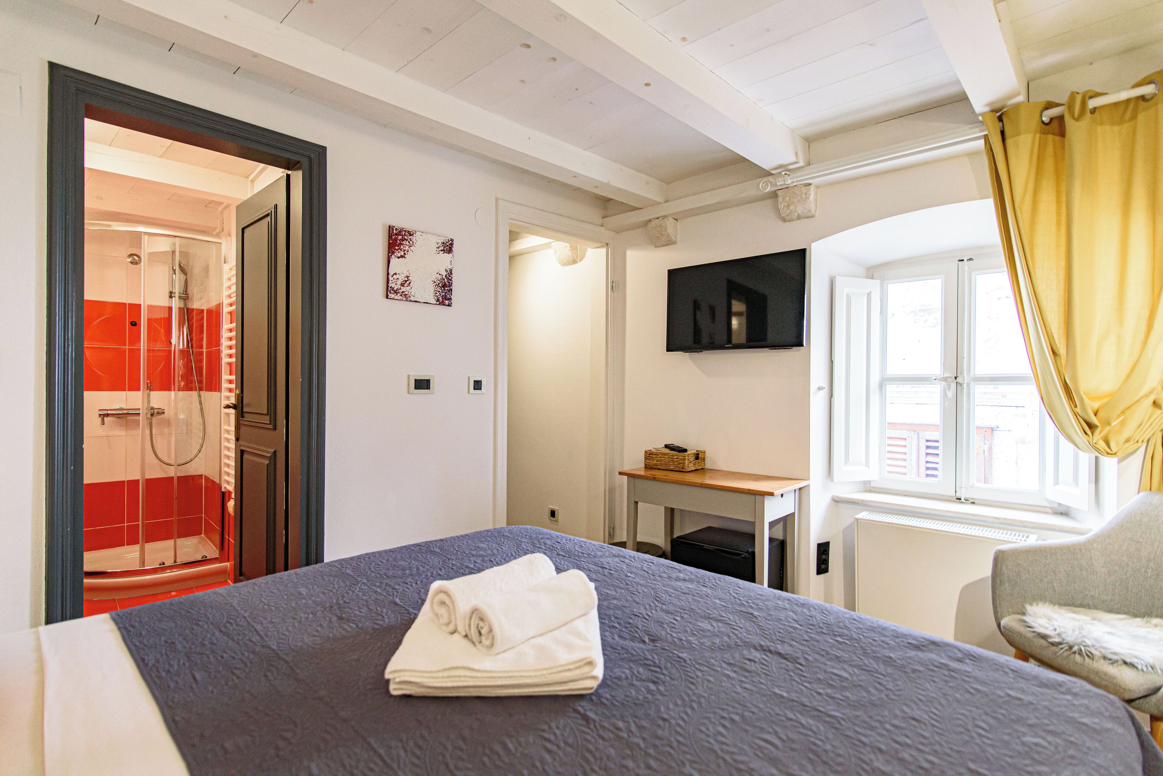 Une chambre d’hôtel avec un lit, une télévision, une fenêtre avec des rideaux, un espace douche et une petite table.