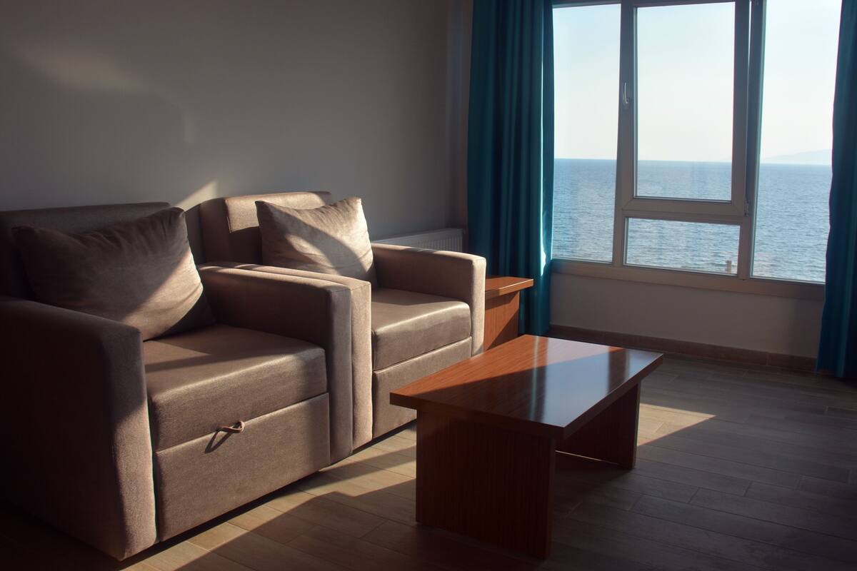 A modern living room with a sofa, a coffee table, and a view of the sea through a window.