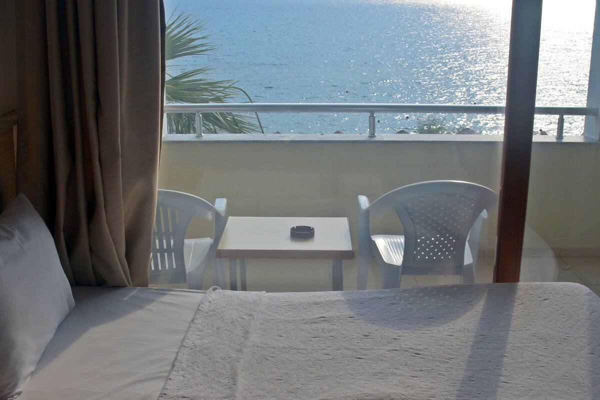 A hotel room with a bed, a table, and chairs. The room has a view of the sea.