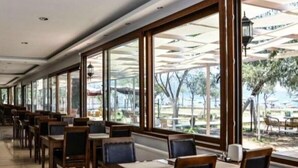 Un restaurant amb taules llargues i caires, finestres grans i ombrel·les exteriors.