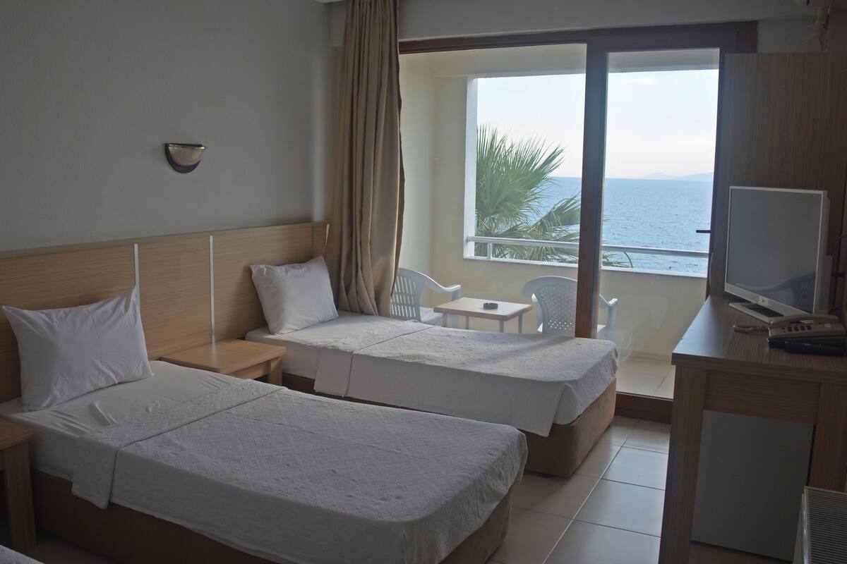 A hotel room with two beds, a desk, a chair, and a view of the sea.