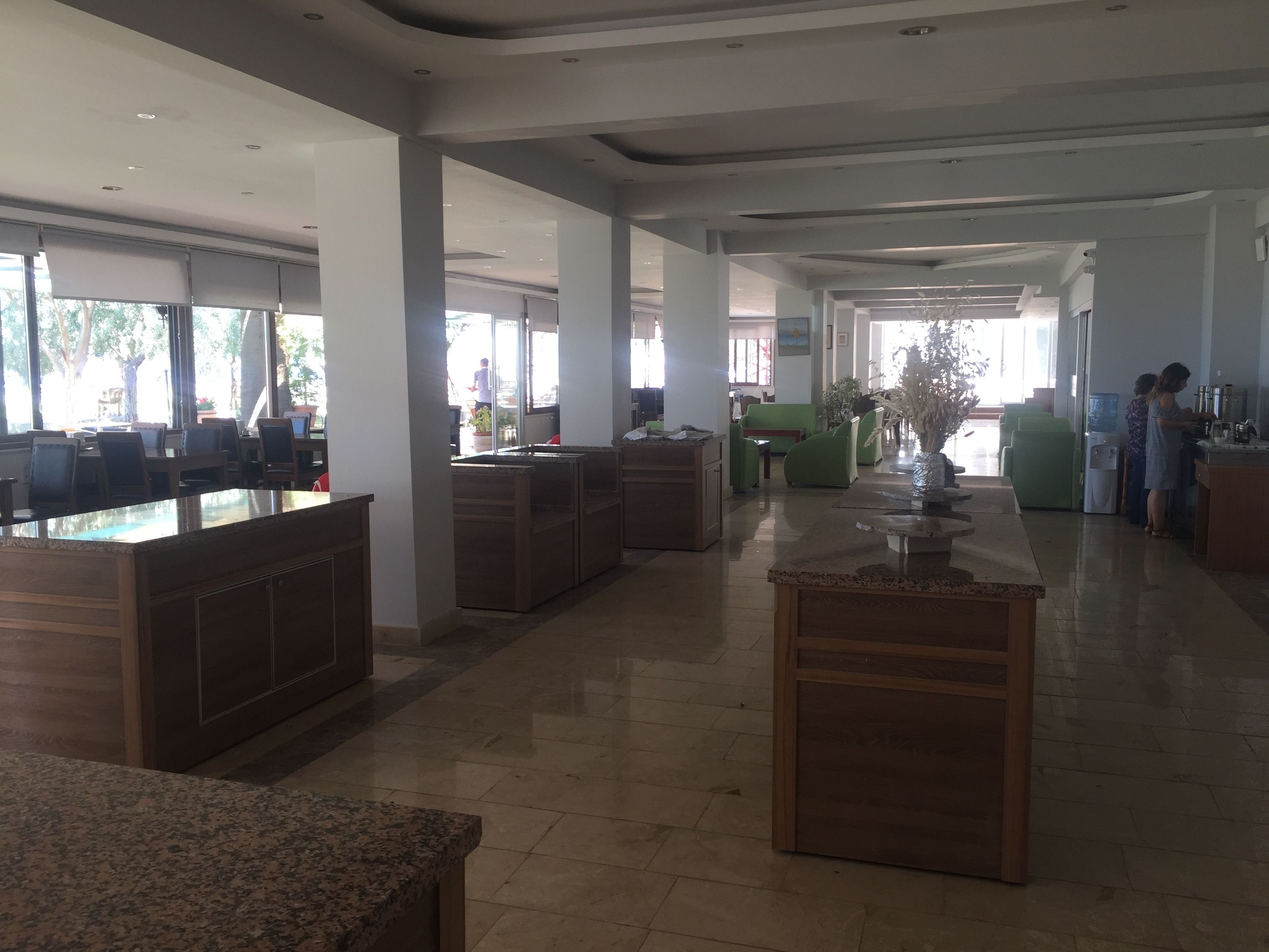 A spacious hotel lobby with a central reception desk, seating areas, and a view of the outdoors.