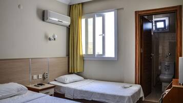 Une chambre d’hôtel avec deux lits simples, une fenêtre avec des rideaux, un climatiseur fixé au mur et un espace douche.