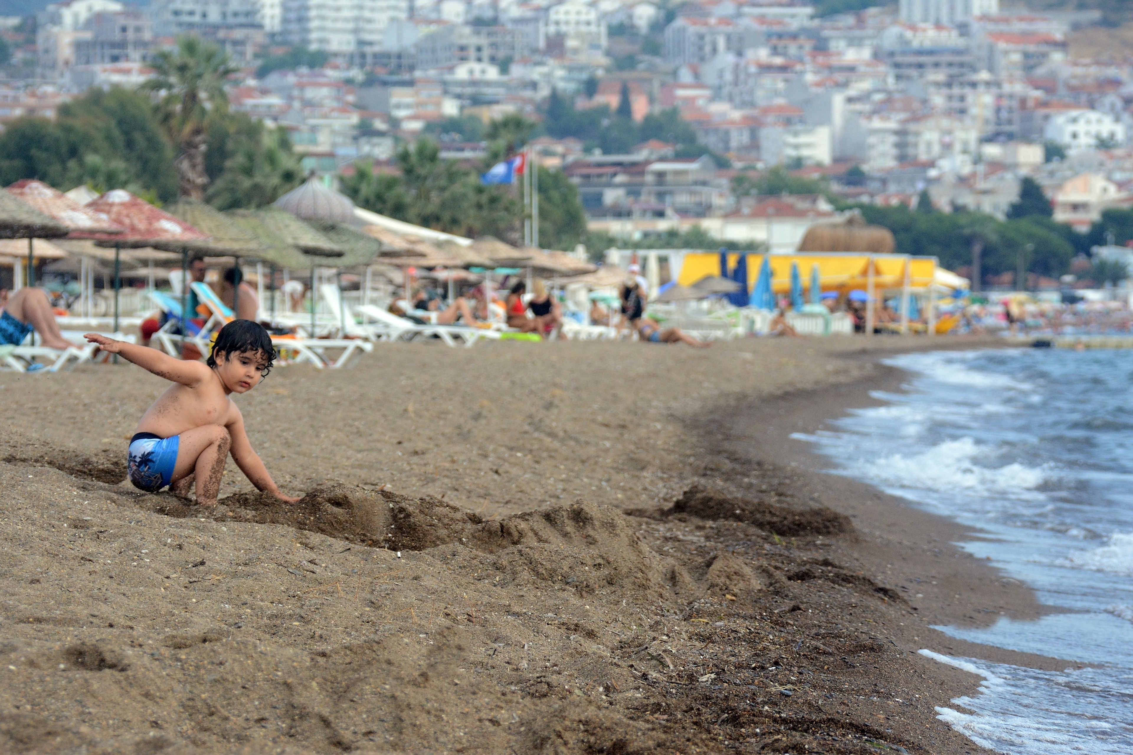 A beach with a child playing in the sand, umbrellas, and beach chairs in the background.