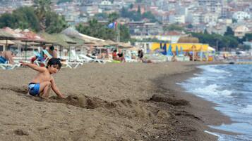 A beach with a child playing in the sand, umbrellas, and beach chairs in the background.