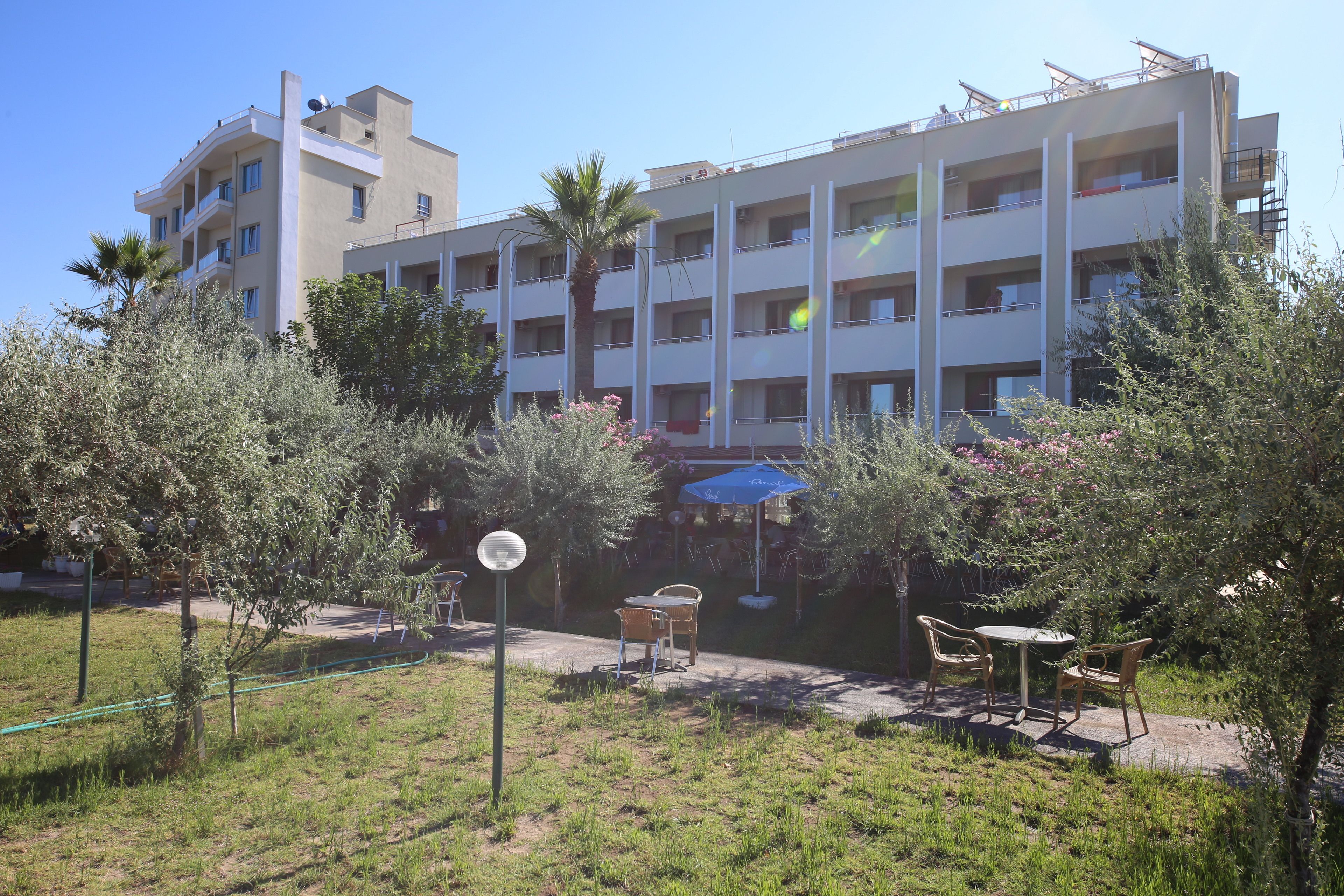 Un edificio de varios pisos con balcones, un jardín con sillas y una mesa, y una palmera.