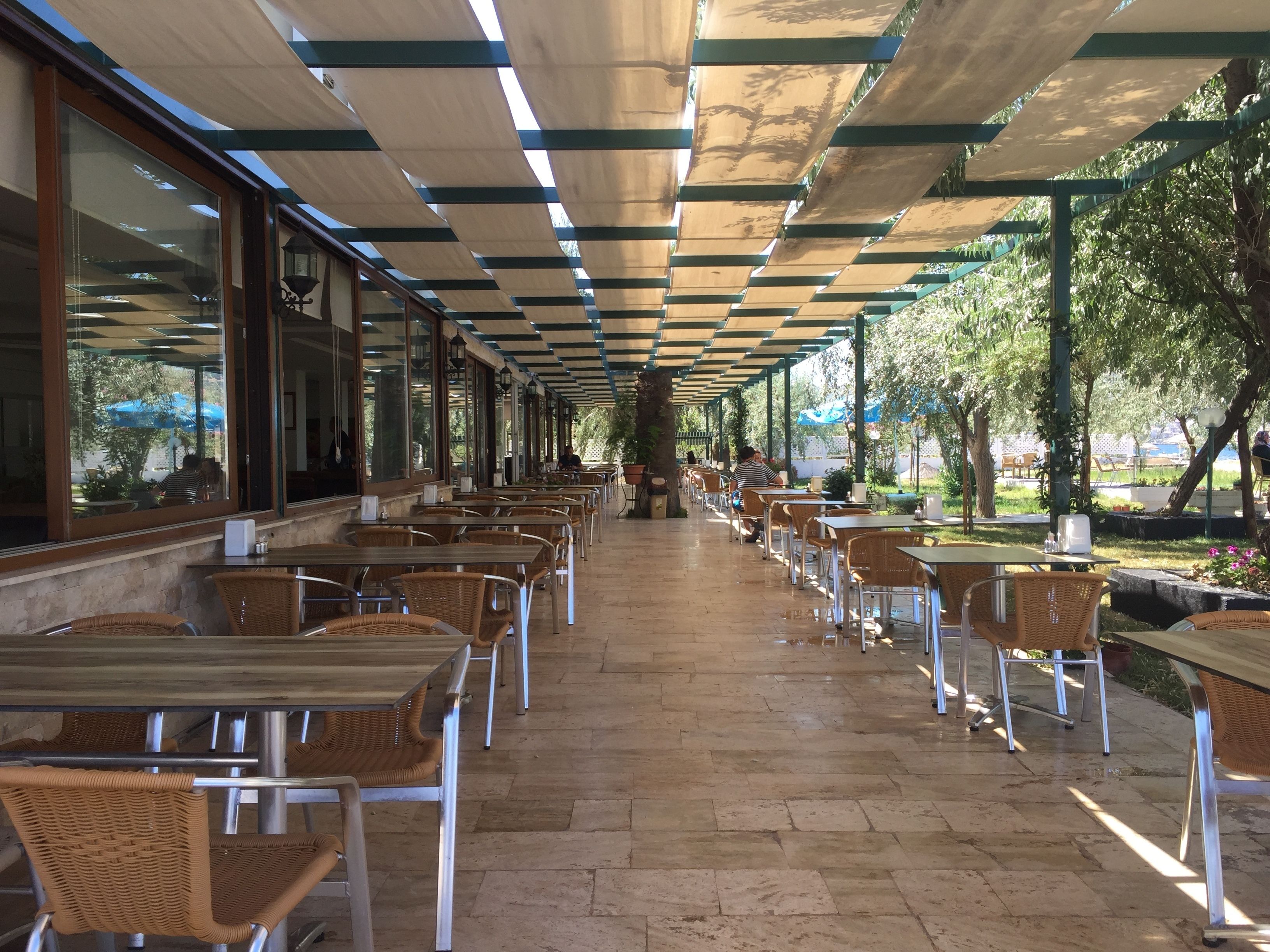 An outdoor cafe with rows of tables and chairs, large windows, and a covered walkway.