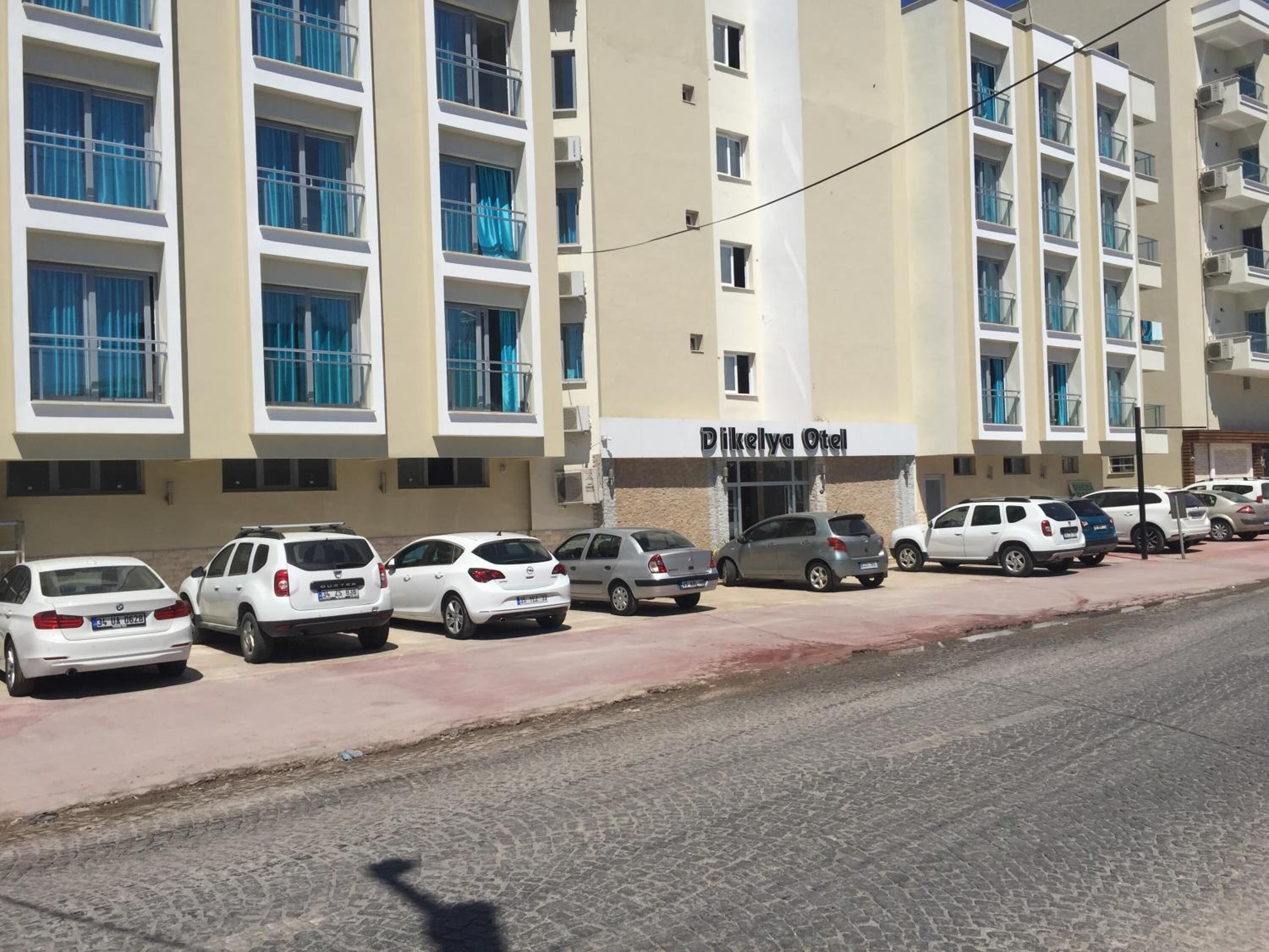 A multi-story hotel with a sign reading "Dikelya Otel". There are several parked cars in front of the building.