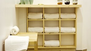 A bathroom with a wooden shelf holding towels and jars.
