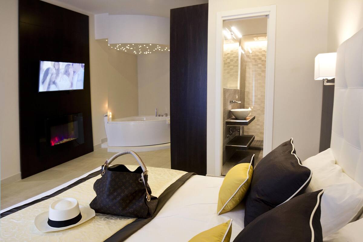 Una habitación de hotel moderna con una cama grande, un televisor de pantalla plana, una bañera y un baño con espejo y lavabo.