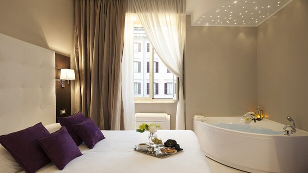 A hotel room with a large bed, a bathtub, and a window with curtains.