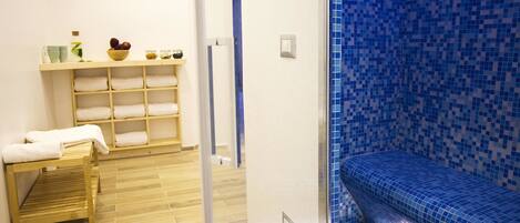 A bathroom with a wooden bench, a shelf with towels, and a blue-tiled shower area.