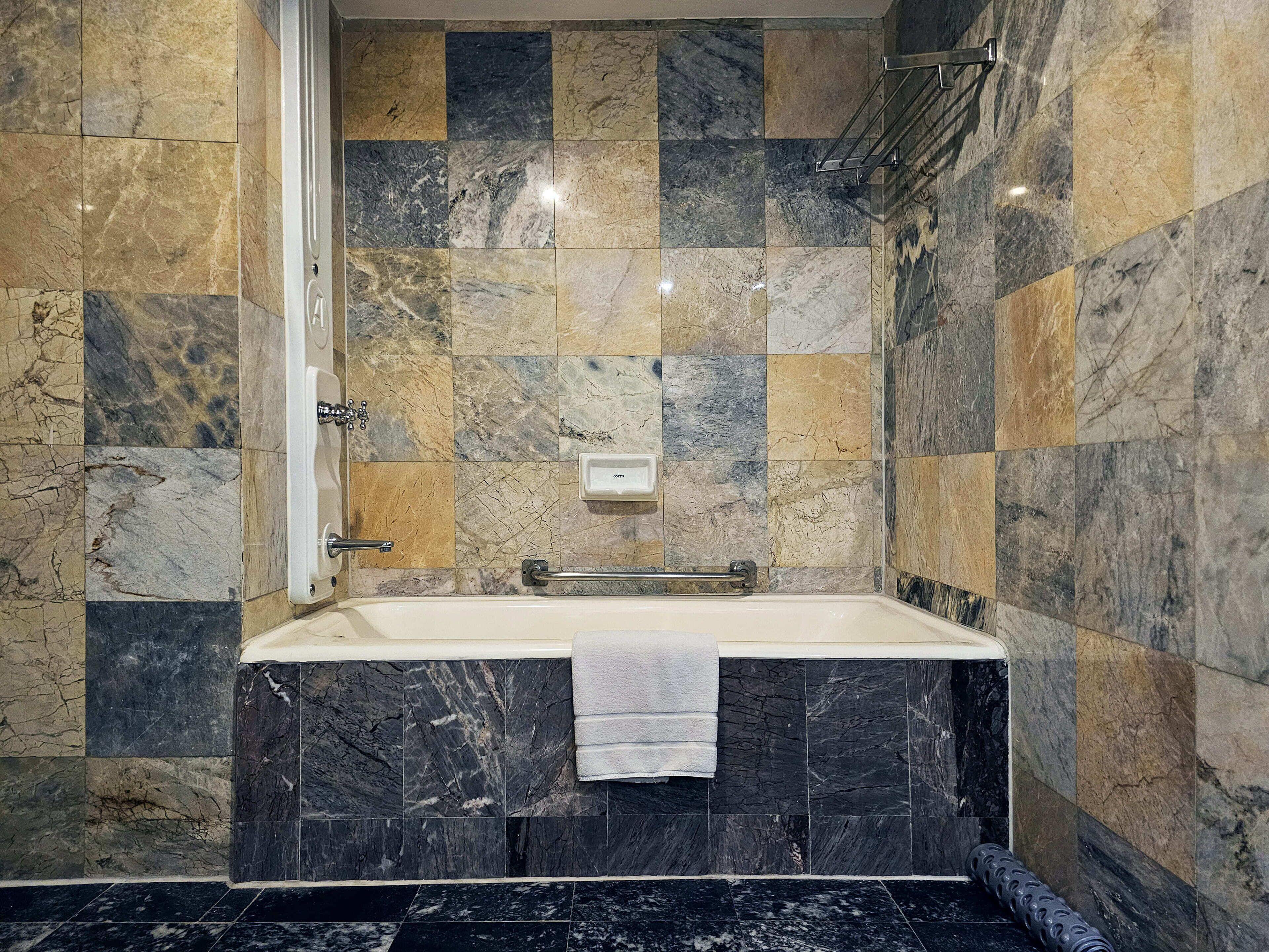 Ein Badezimmer mit Marmorplatten, einer Badewanne und einem Handtuchhalter.