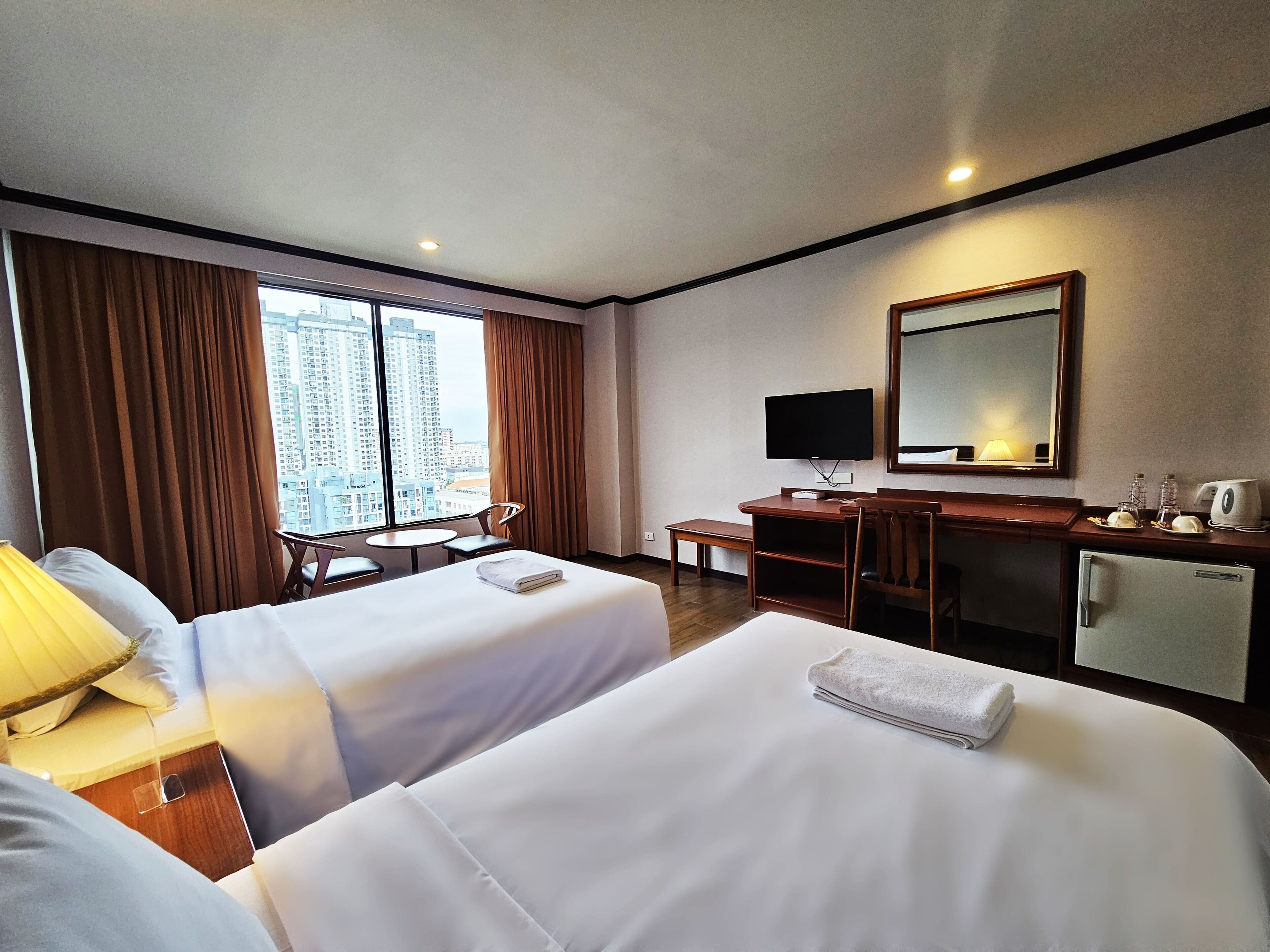 A hotel room with two beds, a desk, a television, and a view of tall buildings.