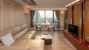 A modern living room with a sofa, chairs, a coffee table, a TV, and a large window with a city view. - Alexander Hotel (Bangkok)
