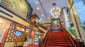 A grand staircase with red carpeted steps leading to a balcony with ornate railings. - Alexander Hotel (Bangkok)
