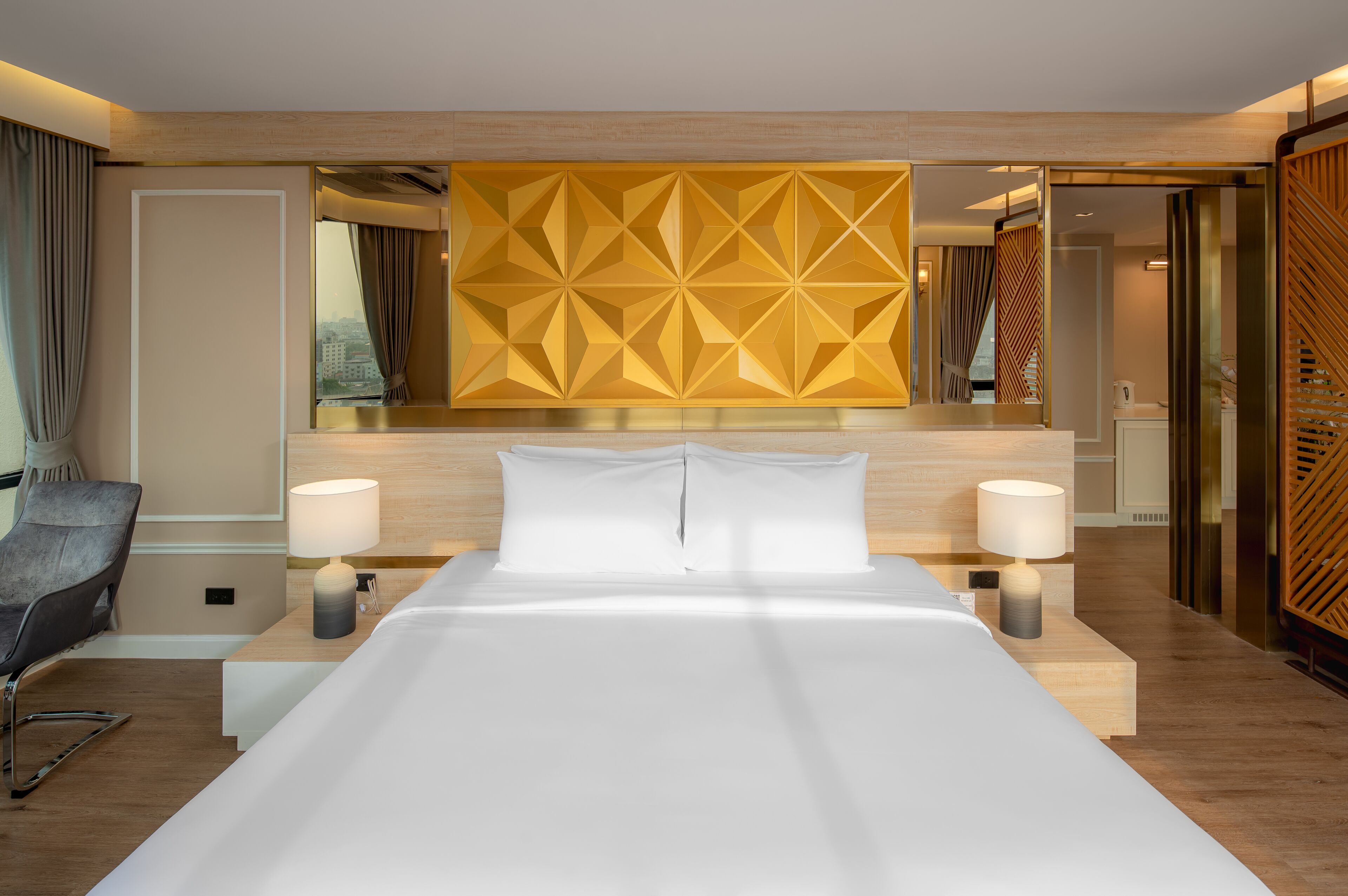 A hotel room with a large bed, two bedside tables with lamps, a chair, and a geometric patterned wall.