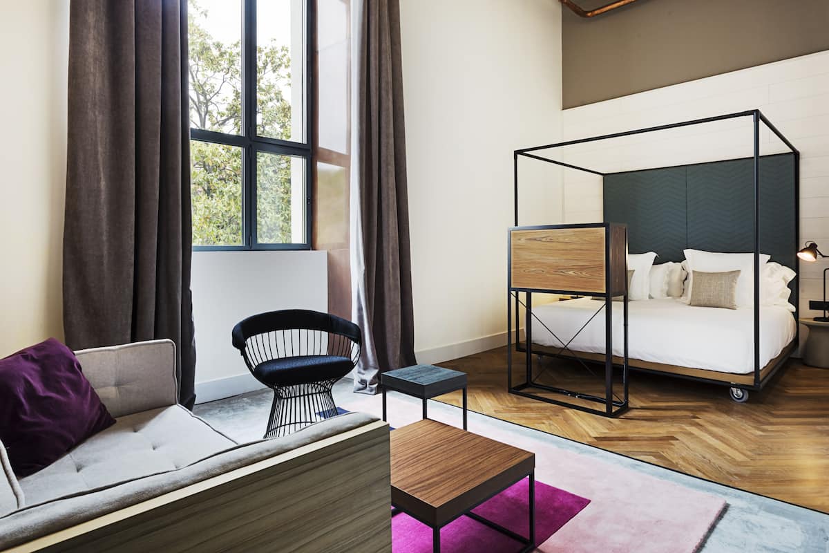 A modern bedroom with a sofa, a chair, a small table, and a canopy bed.