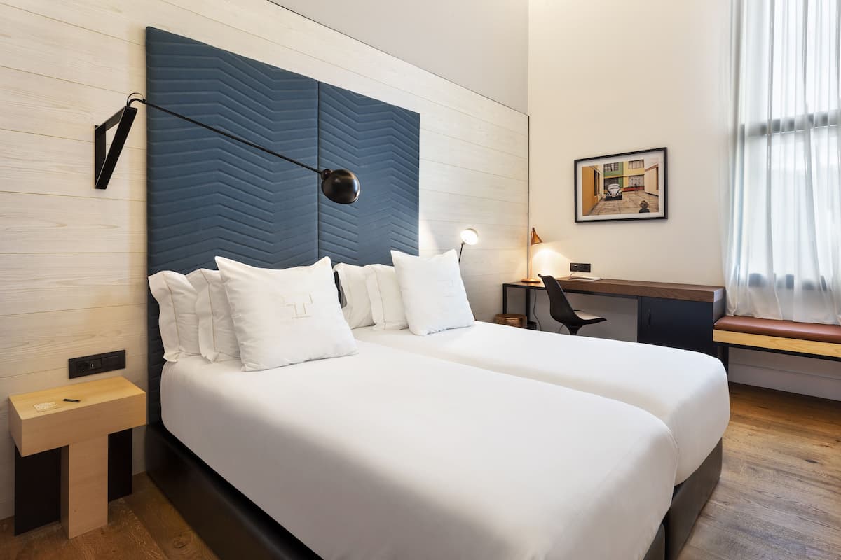 A modern hotel room with a large bed, a desk, and a small bedside table.