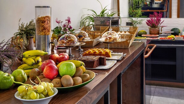 A buffet table with various fruits, pastries, and a decorative plant arrangement. - One Shot Tabakalera House (San Sebastián)