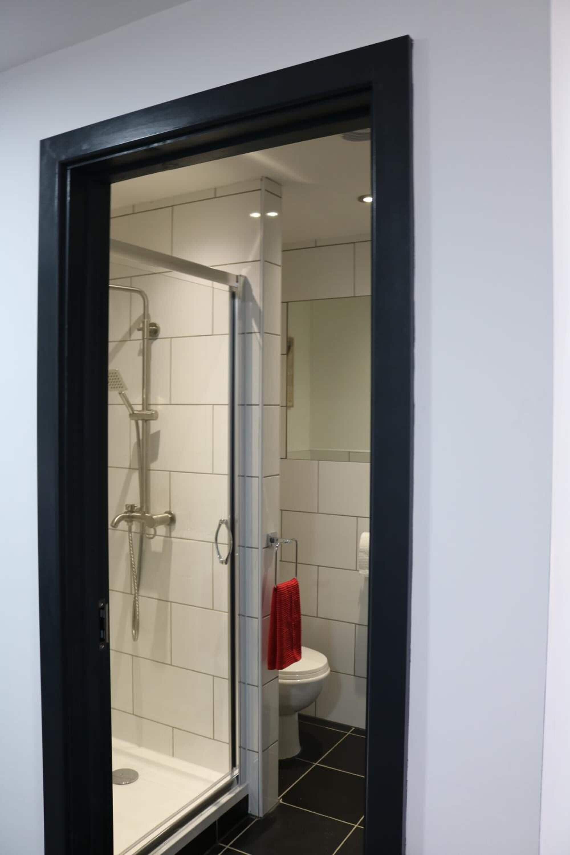 A modern bathroom with a glass-enclosed shower, white tiles, a white toilet, and a red towel hanging on the wall.