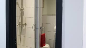 A modern bathroom with a glass-enclosed shower, white tiles, a white toilet, and a red towel hanging on the wall.